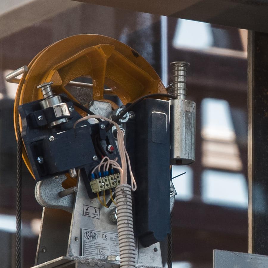 Elevator overspeed governor mounted on its bracket in a shaft, with the cast sheave, centrifugal trip mechanism and governor rope running taut over it